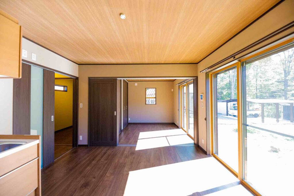 山梨県で建てたコンパクトな平屋住宅のLDK。木目の天井と濃いフローリング、大きな掃き出し窓で明るく開放的な空間が広がる。