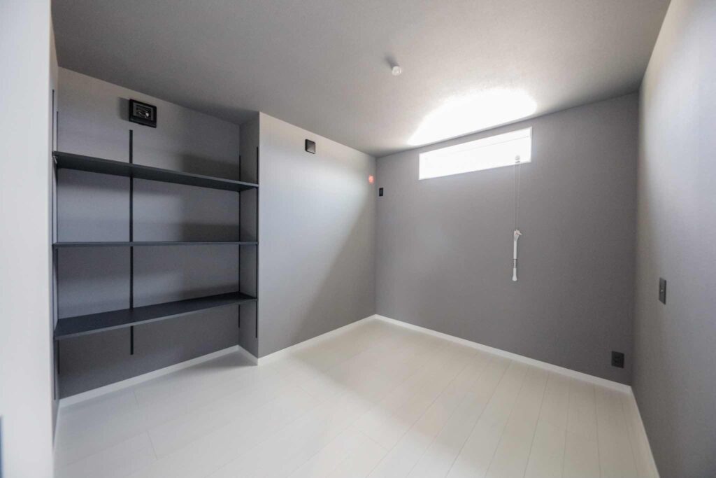 山梨平屋専門店が建てた住宅の一室。グレートーンの壁と天井、白い床、オープンシェルフ収納を備えた落ち着いたデザイン空間。