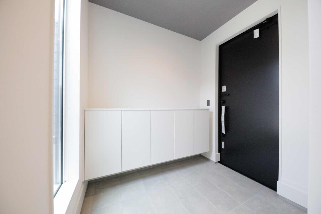 山梨平屋住宅の玄関。白いフロート収納と黒い玄関ドアが特徴のモダンで明るい空間