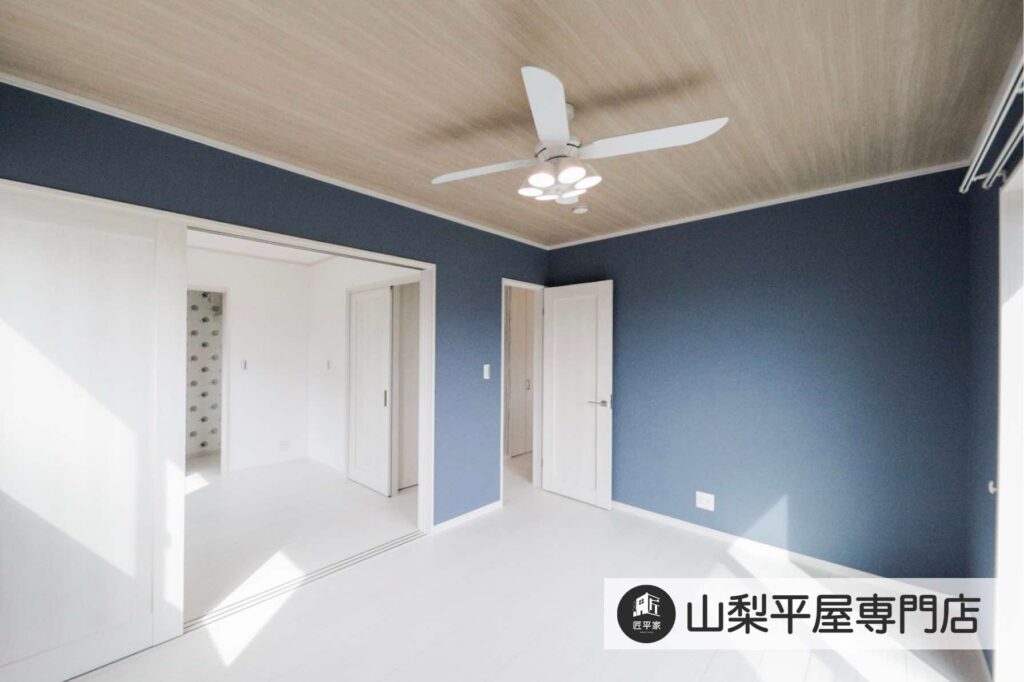 ブルーの壁と木目天井、シーリングファン付き照明を採用した山梨平屋住宅の居室施工事例