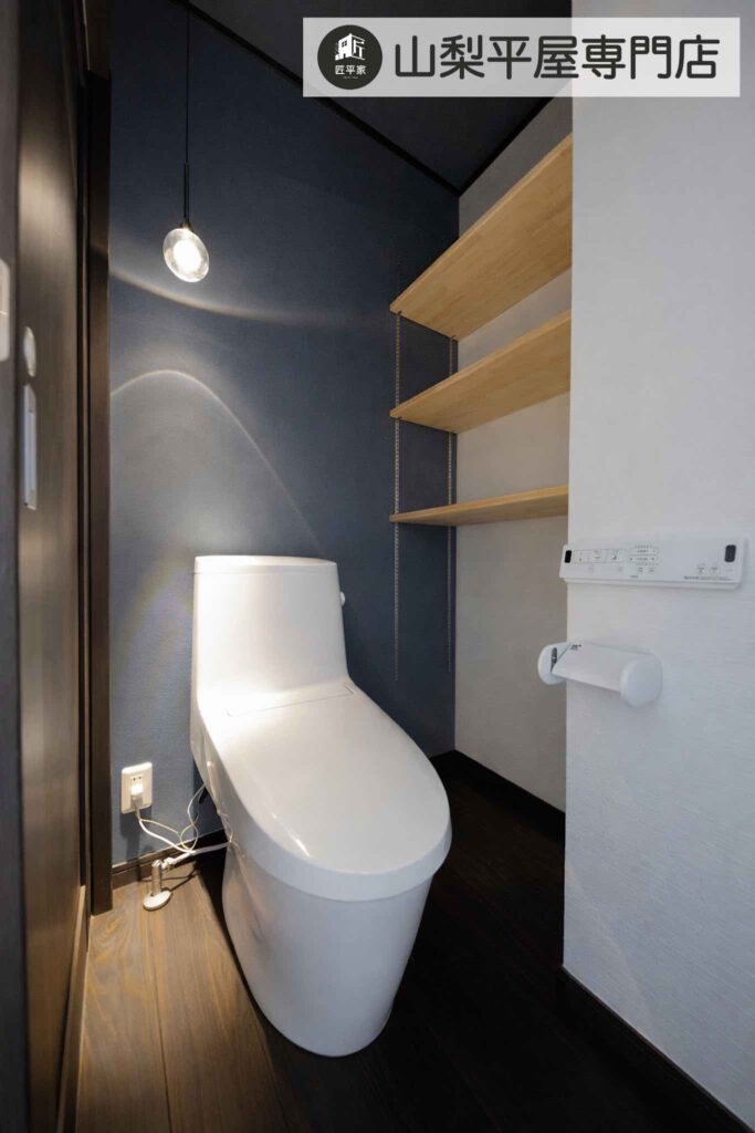 ブルーのアクセントクロスとペンダントライト、木製棚を採用した山梨平屋住宅のトイレ施工事例