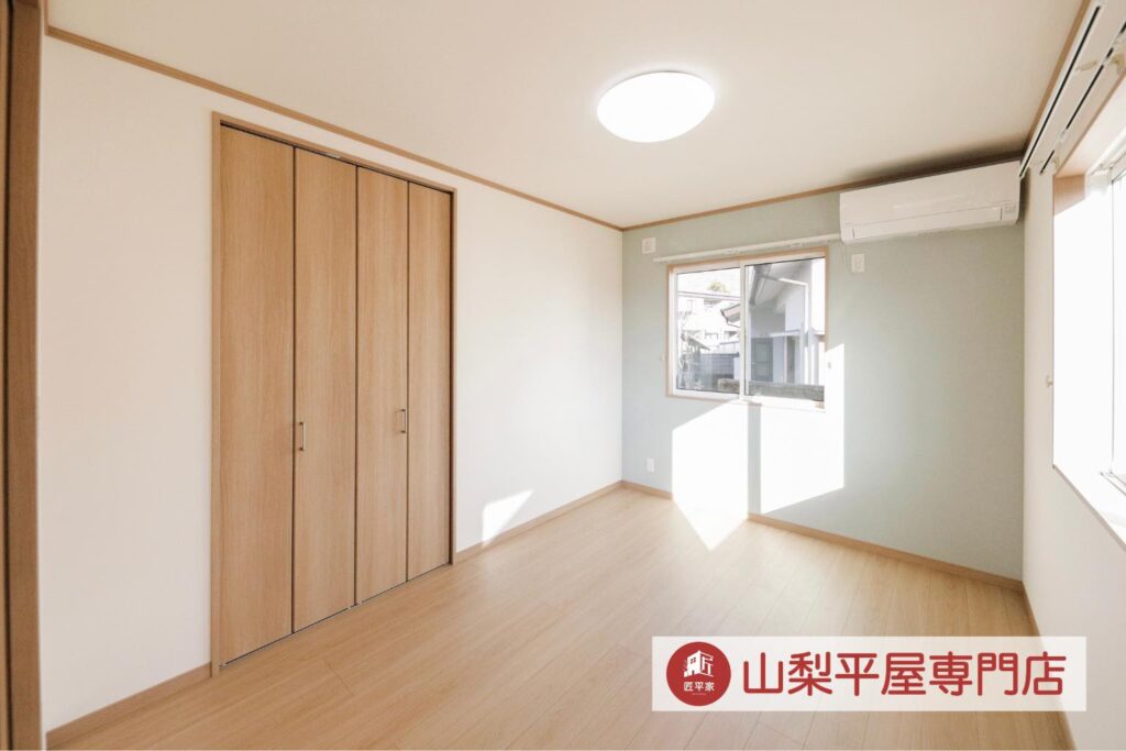 淡いグリーンのアクセントクロスと木目の収納を採用した明るい山梨平屋住宅の居室